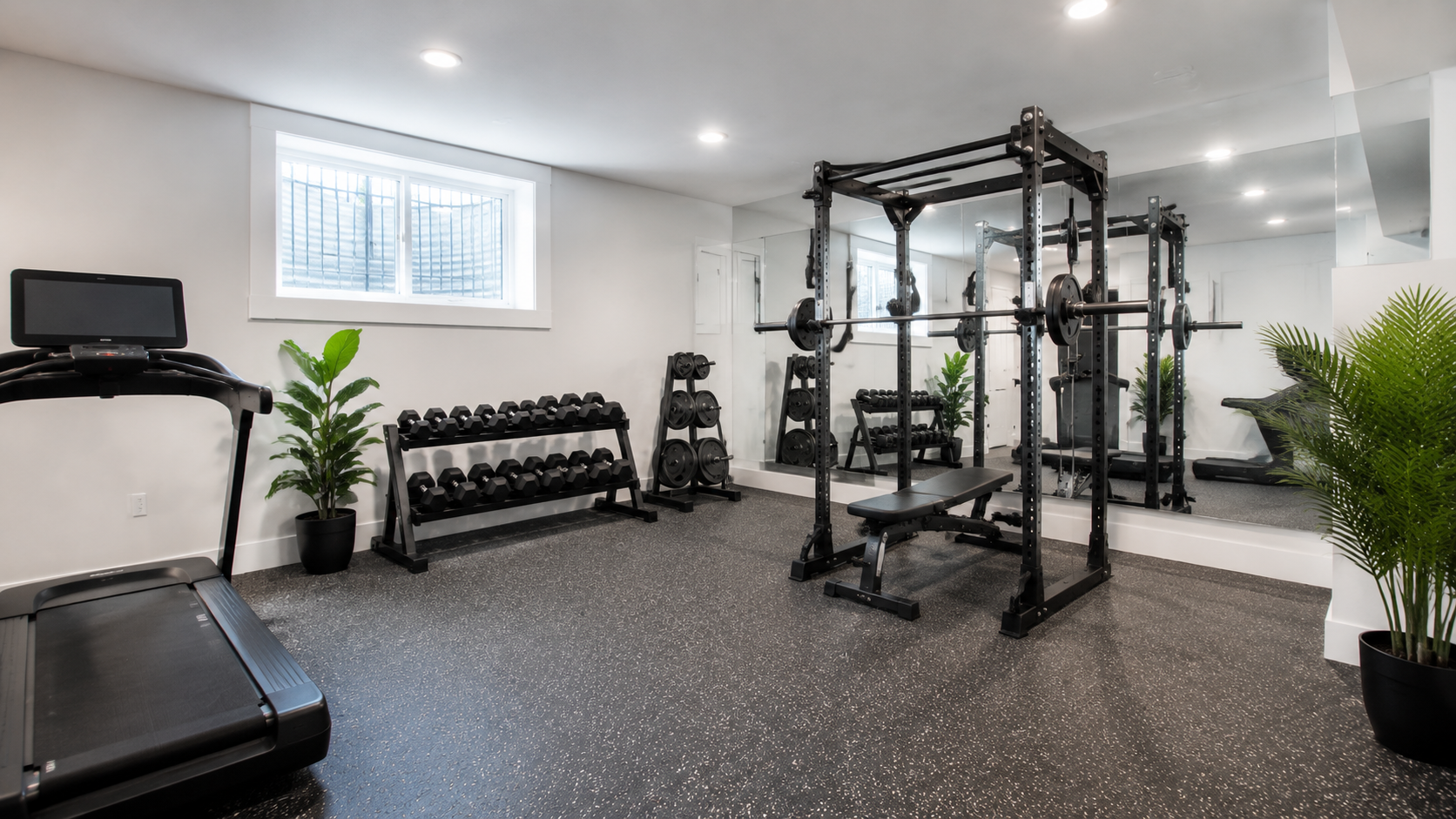 Finished basement home gym with rubber flooring, a mirror wall, and a squat rack